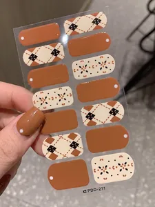 Close-up of caramel checkered nail stickers with floral patterns on a finger
