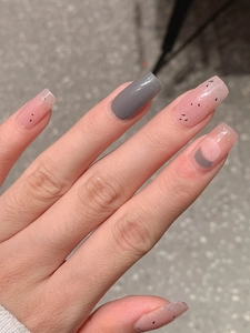Detailed view of glossy light pink press-on nails with black ink spots and dark grey accent
