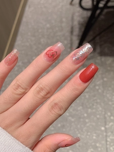 Détail de faux ongles rouges et roses pailletés avec motifs de cœurs et fini brillant