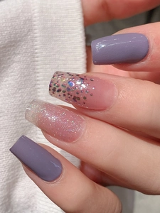 Nahaufnahme von violetten Glitzer-Nagelstickern auf eckigen Nägeln mit Strickhintergrund