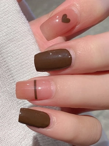 Detail of short square brown nails with heart patterns and stripes on a knit background