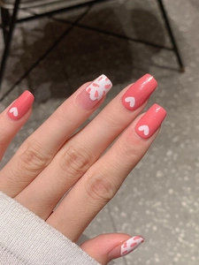 Close-up of pink heart pattern press-on nails with glossy coral finish in natural light