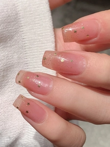 Détail d'ongles autocollants dégradé rose avec paillettes dorées et motifs d'étoiles