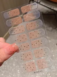 Détail de stickers à ongles dégradés rose bleu avec étoiles dorées et paillettes sur main