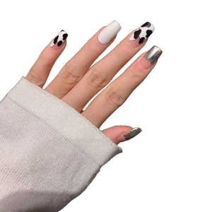 Autocollants à ongles motif vache et argent holographique sur main avec pull blanc