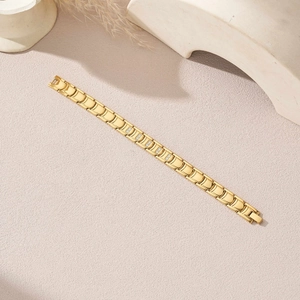 Détail d'un bracelet à maillons en acier doré avec zircone sur un fond de sable