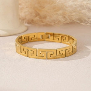 Detail of golden stainless steel bracelet with Greek Key pattern and brushed texture