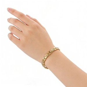 Eleganter goldfarbener Armreif mit Kreuzmuster und funkelnden Steinen am Handgelenk