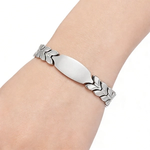 Detailed view of silver wheat chain bracelet with polished oval plate on model's wrist