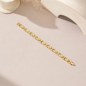Makro-Detail eines goldenen Gliederarmbands mit eingelegten Steinen auf sandigem Grund