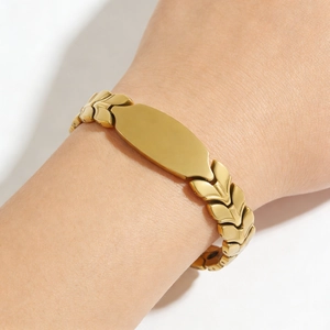 Macro shot of gold wheat-link bracelet with oval metal plaque on woman's wrist
