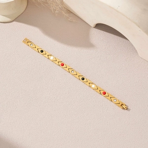 Details eines goldenen Edelstahl-Armbands mit bunten Steinen auf sandigem Hintergrund