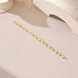 Bracelet magnétique doré en forme de X avec maillons losanges sur fond rose poudré