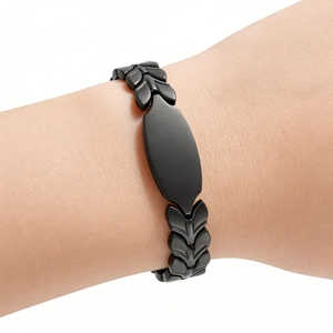 Detail of matte black wheat link bracelet with custom oval plaque on a model wrist
