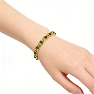 Gros plan d'un bracelet doré orné de zircons ronds vert émeraude porté au poignet délicat