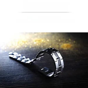 Detail of stainless steel men's bracelet with Greek key pattern on black wood surface