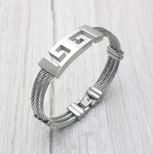 Detail showing the braided stainless steel cable texture and Greek key pattern on the bracelet