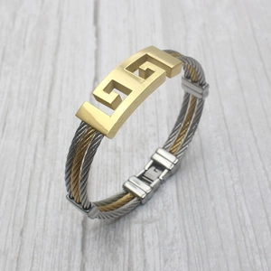 Macro detail of stainless steel cable bracelet with gold-plated geometric fretwork