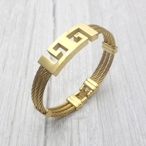 Macro shot of gold twisted steel cable bracelet featuring a Greek key pattern clasp