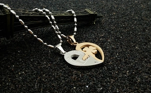 Detail view of heart-shaped puzzle necklaces in silver and rose gold over black sand
