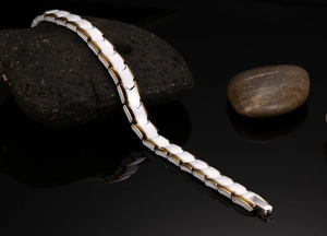 Detail of white ceramic and gold metal linked bracelet on natural stone background