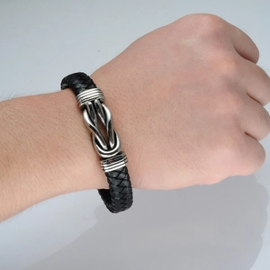 Close-up of men's braided black leather bracelet with polished silver metal knot buckle