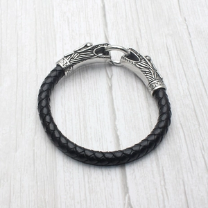 Detail of men's black braided leather bracelet featuring silver dragon head clasps