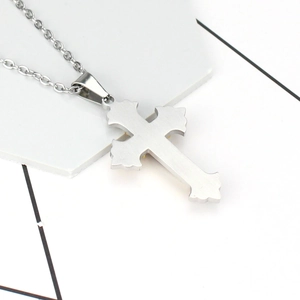 Collier croix classique en acier titane brossé avec bords décoratifs sur un socle blanc