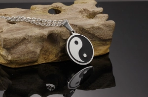 Macro detail of Tai Chi Yin Yang pendant on rustic wood over black mirror surface