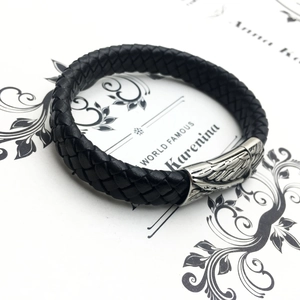 Close-up of black braided leather bracelet featuring a silver wing engraved metal clasp