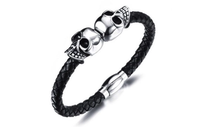 Detail of black braided leather bracelet featuring double skull charms and magnetic clasp
