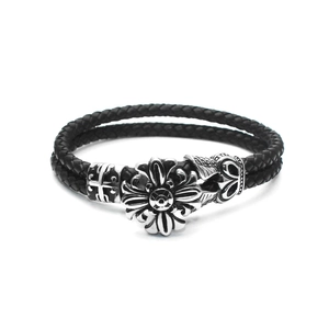 Detail of woven black leather bracelet with vintage silver sun floral and cross charms