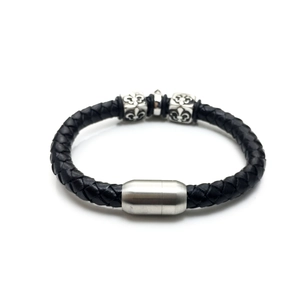 Detail of black woven leather bracelet featuring silver fleur-de-lis beads and magnetic clasp