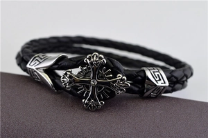 Detail of a punk style black woven leather bracelet with a silver zircon cross charm
