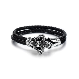 Detail of a braided black leather bracelet featuring a silver fleur-de-lis metal charm