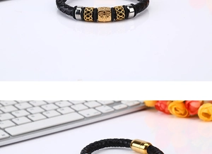 Macro detail of men's black braided leather bracelet featuring a golden Fleur-de-lis bead