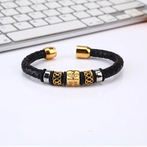 Men's woven leather bracelet with gold cross bead and magnetic clasp on keyboard