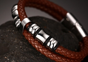Detail of brown braided leather bracelet with silver metal charms and magnetic clasp