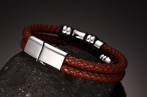 Detail of brown braided leather bracelet with magnetic metal clasp on dark rock surface