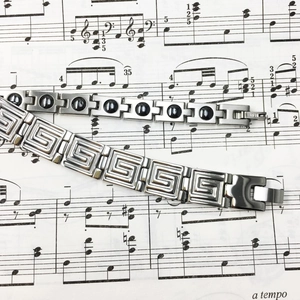 Detailed view of titanium steel bracelets with meander pattern and black stone on sheet music