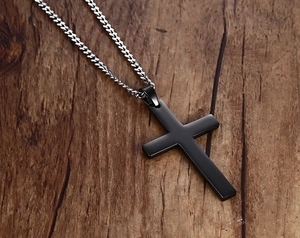 Gros plan d'un pendentif croix noir mat sur une chaîne argentée sur fond en bois