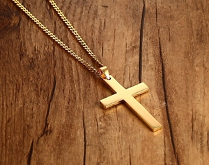 Pendentif croix doré poli avec chaîne gourmette sur fond en bois sombre