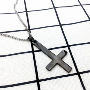 Détail d'un pendentif croix inversée noir mat avec une chaîne gourmette argentée sur damier