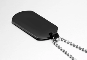 Macro view of matte black dog tag pendant with silver bead chain on a brushed metal surface