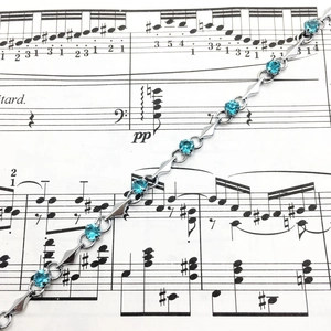 Close-up of light blue zircon bracelet with silver geometric links on musical score