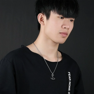 Close-up of a silver anchor pendant on a steel chain worn by a male model on black backdrop