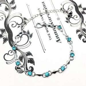 Detailed close-up of a silver bracelet with sky blue zircons and a small bell charm