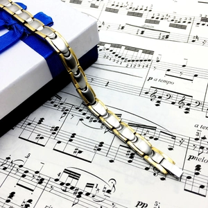 Polished gold and silver titanium steel health bracelet on a gift box over music sheet
