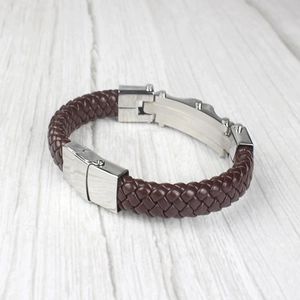 Bracelet tressé pour homme en cuir marron avec boucle en acier argenté sur fond bois blanc