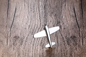 Macro shot of a polished silver airplane pendant necklace on a natural wood background
